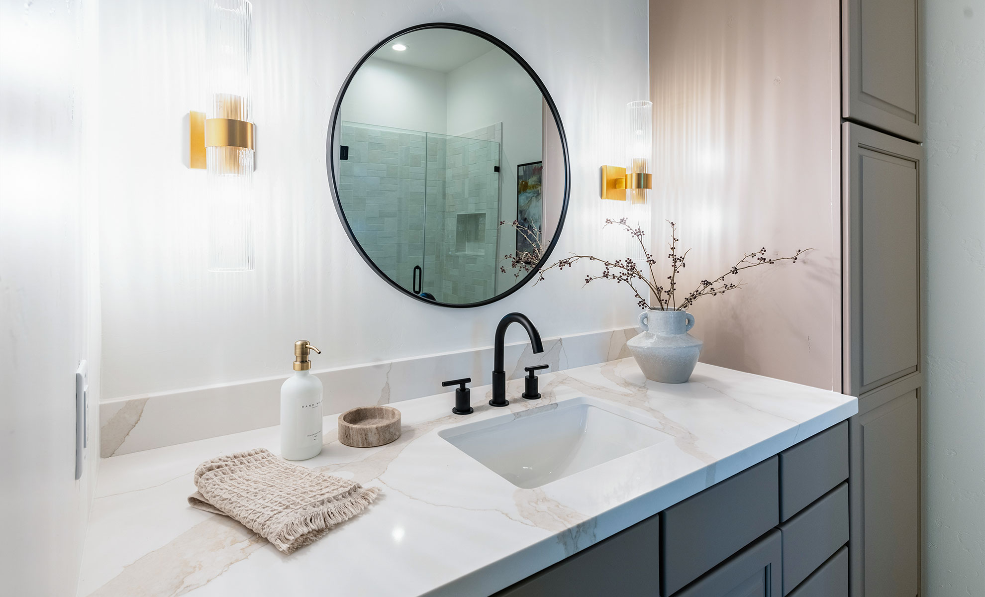 This image depicts a guest bath featuring a quartz bathroom countertop featuring a white background with bold, dynamic gold and grey veining. The sleek surface is complemented by modern black hardware.